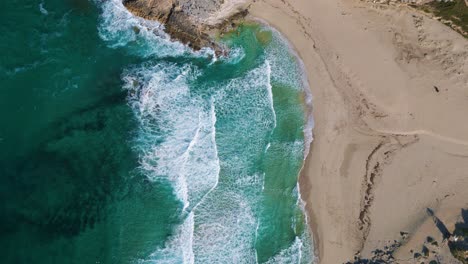 Bird-view-beach-bay-with-waves,-clear-turquoise-sea-water,-green-hills,-white-sand