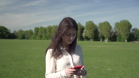 Happy-smiling-gorgeous-italian-girl-enjoying-walking-around-the-park-while-typing-text-via-smartphone-gadget,-positive-female-tourist-using-technology-to-communicate