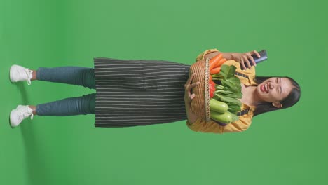 woman holding a basket of vegetables and using a phone