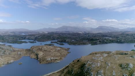 sideways aerial of a vast lake with multiple islands in an overwhelming mountainous scottish region