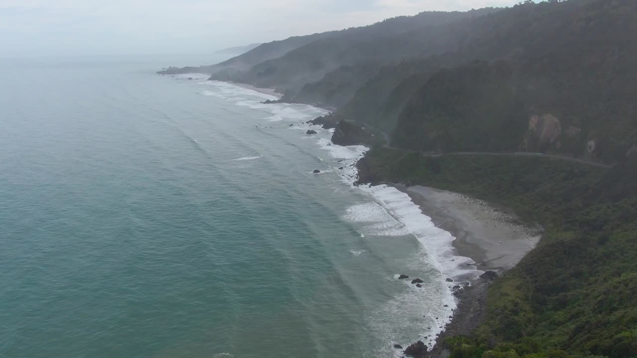 Costa occidentale della Nuova Zelanda con onde che si infrangono sulla riva accanto all'autostrada.