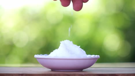 mano de la gente agarra sal de cristal blanco en el cuenco y verterlo