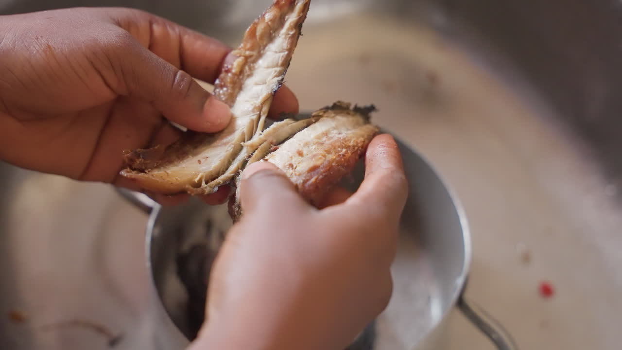 Closeup black hands cleaning fish in stainless sink, removing scales and guts into small pan, gentle natural light, tactile motions and careful grip, home cook preparing family meal with focused skill