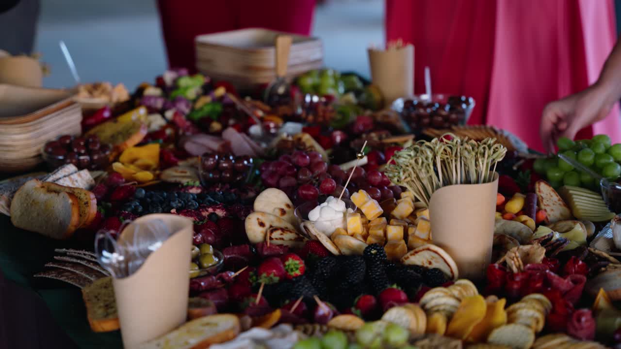 A vibrant charcuterie table during the cocktail hour at a fall wedding. A guest reaches for a bite from a spread filled with fruits, cheeses, and artisanal snacks at a rustic winery venue