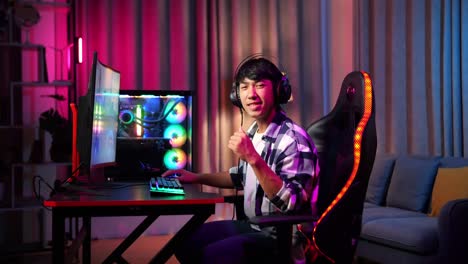 asian teen boy gamer smiling to camera and showing thumb up while playing video game on computer
