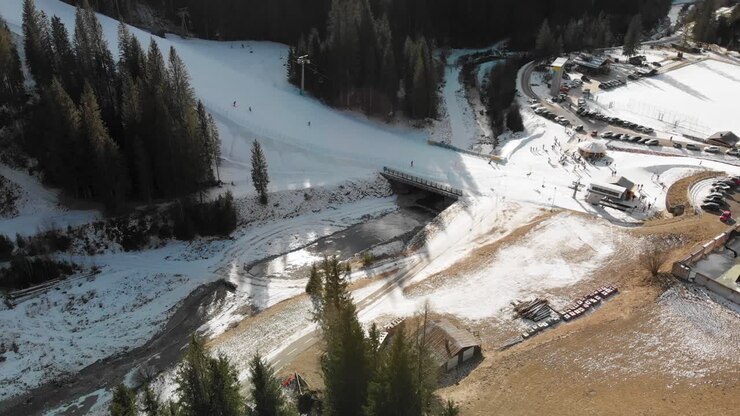 Panoramica aerea in salita di persone che sciano lungo un pendio sul comprensorio sciistico di Sappada in Italia, con riflessi solari.