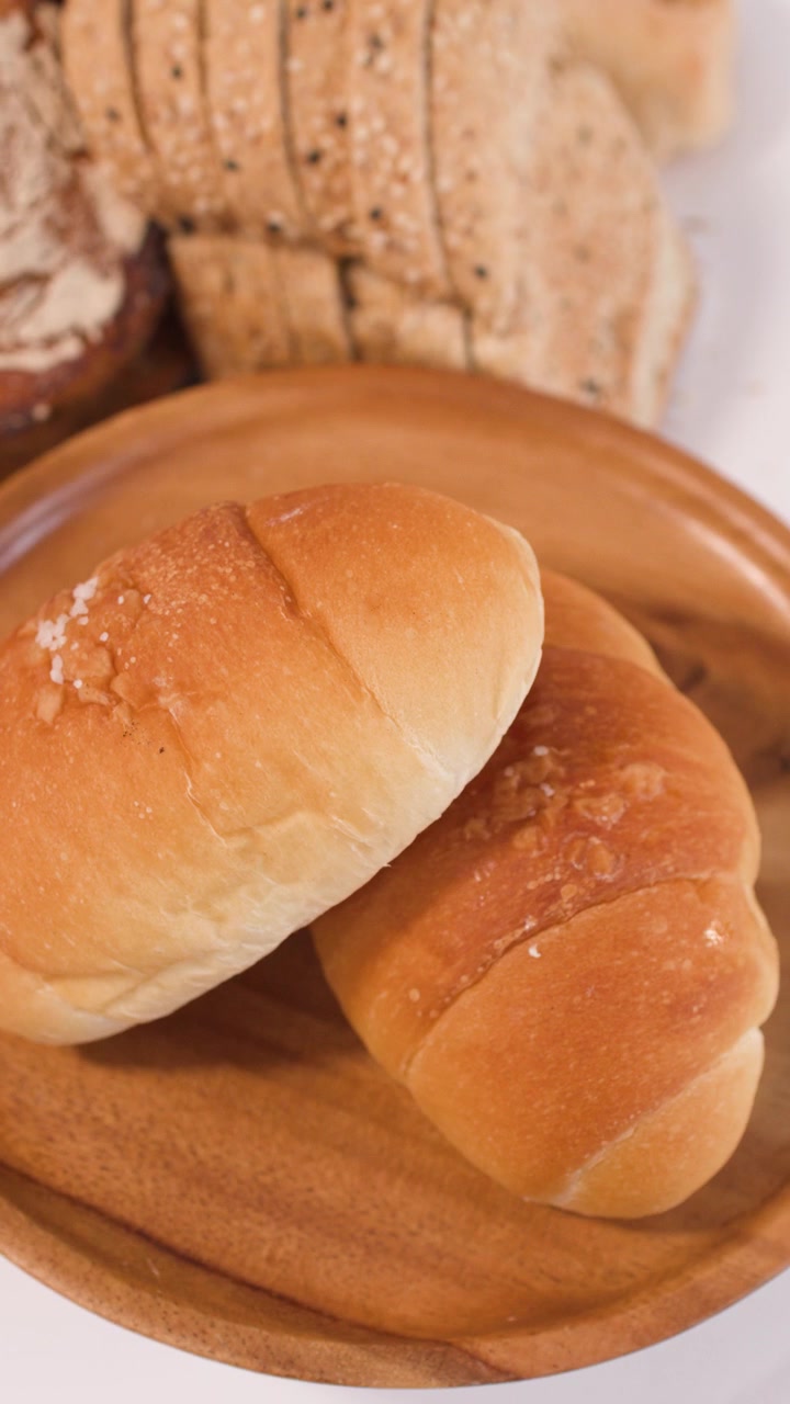 Plano panorâmico em close-up de pão de fermentação natural, croissants e pão integral fatiado em pratos de madeira