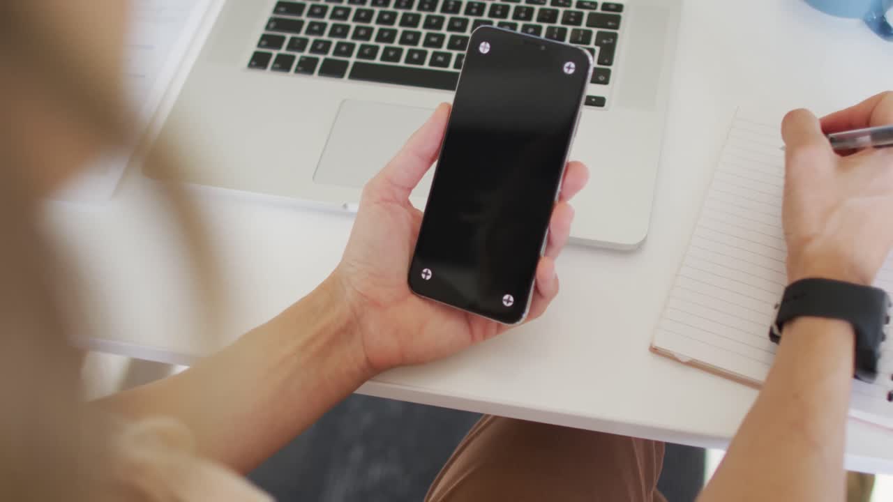 책상 에 앉아 스마트폰 을 사용 하고 메모 를 하는 백인 사업가