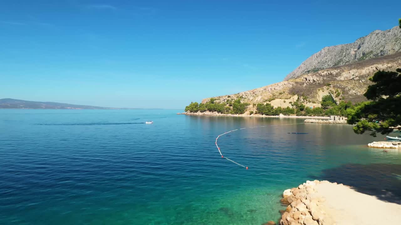 Aerial drone footage following the coastline with pine trees passing boats and swimmers in Mimice, Croatia