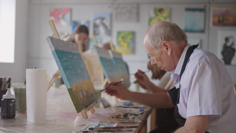 Una-Joven-Profesora-Ayuda-A-Un-Anciano-Jubilado-A-Aprender-A-Pintar-Un-Cuadro.-Hombre-Mayor-Aprendiendo-A-Dibujar