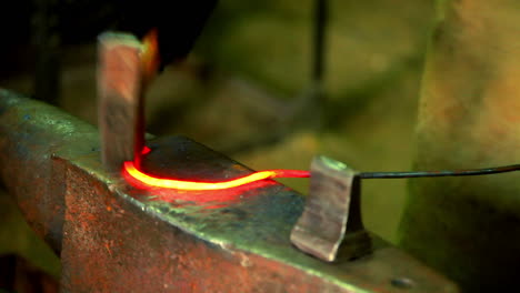 herrero formando hierro caliente rojo en gancho en el yunque. metal caliente en el yunque en el taller