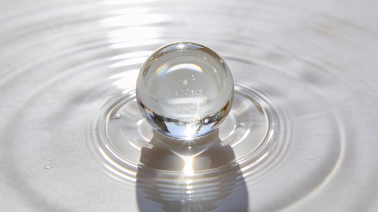 En oscillerende glaskugle skaber koncentriske ringe på en hvid skål og kaster en lys refleksion.