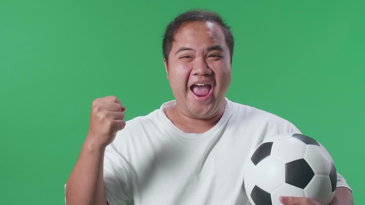 푸른 스크린 배경에서 축구를 응원하는 동안 우승 팀을 축하하는 골을 외치는 공을 가진 아시아 남자의 클로즈업
