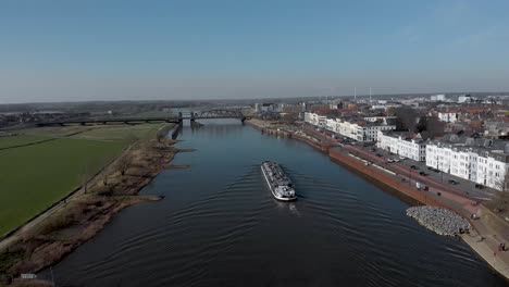 following a large container cargo ship passing by embankment of historic medieval hanseatic city of zutphen, the netherlands, besides river ijssel