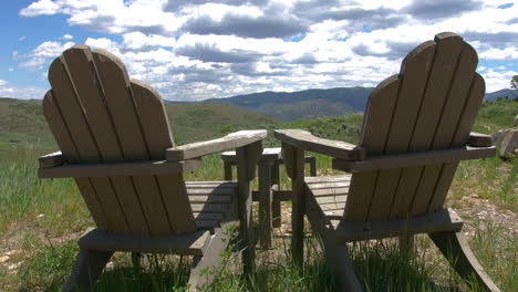 a shot of two wooden lawn chairs overlooking a vast view of the mountains