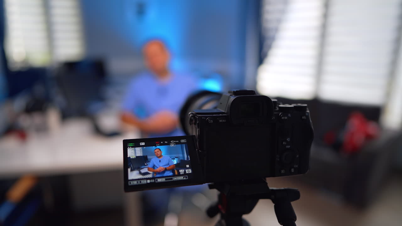 Close look at the display of a digital camera recording a man in blue uniform. Doctor speaks for the video for his medical vlog. Selective focus