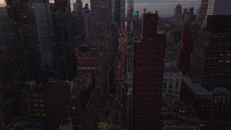 Forwards-fly-above-busy-avenue-in-midtown-at-dusk.-Brake-lights-of-cars-on-street.-Manhattan,-New-York-City,-USA