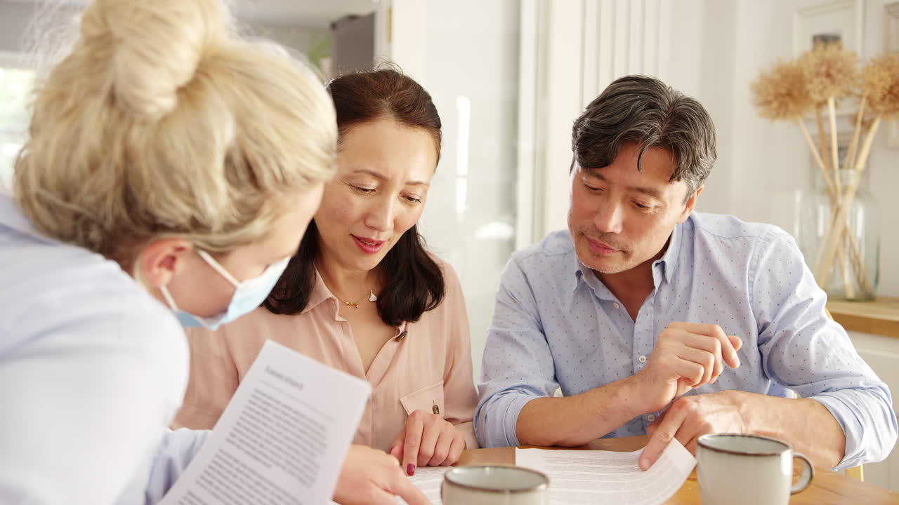 Mature Asian couple at home meeting with female financial advisor in mask during pandemic - shot in slow motion