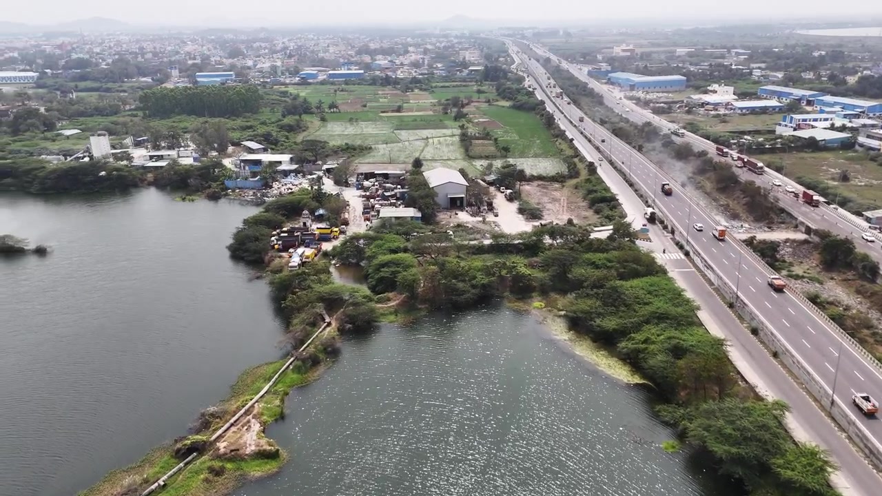 Veduta aerea cinematografica della cava di granito di Sikkarayapuram, con laghi di cava allagati, isole rocciose di granito e la tangenziale di Chennai adiacente. Il paesaggio mette in mostra la natura e il patrimonio minerario.
