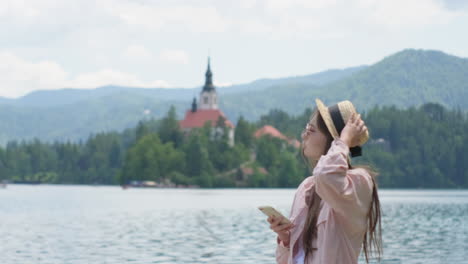 woman with phone on a lake, mountains in the background