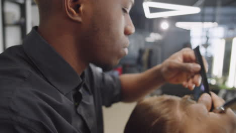 black hairdresser combing wet hair of client in barbershop