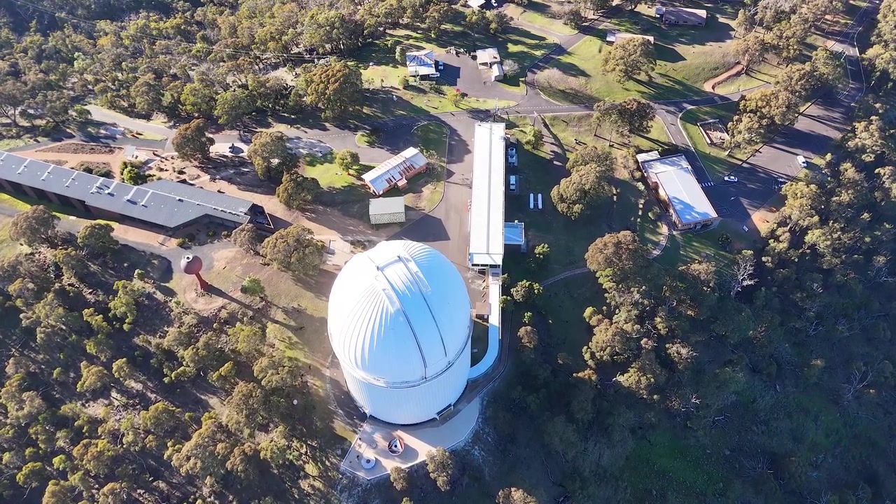 Toma aérea de gran angular de una cúpula de telescopio blanca en el Observatorio Siding Spring, Australia.