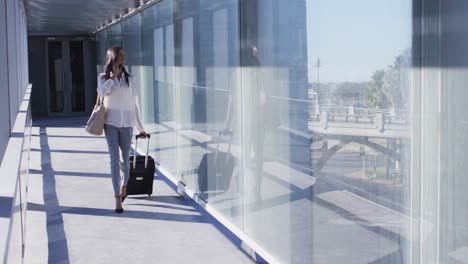 video of biracial woman walking with suitcase and using smartphone