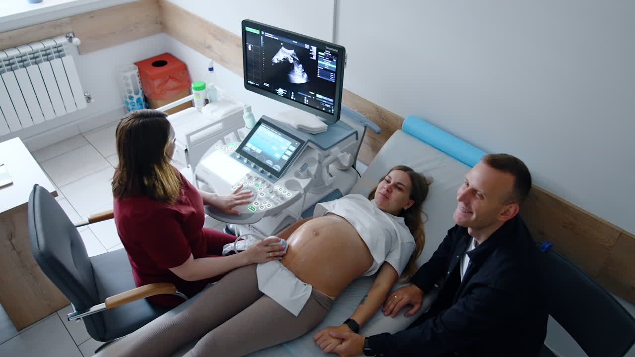 Happy smiling Caucasian couple expecting a baby having ultrasound check. Excited people see their future child on the monitor. Top view.