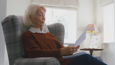 worried senior woman at home looking at energy bill during cost of living energy crisis