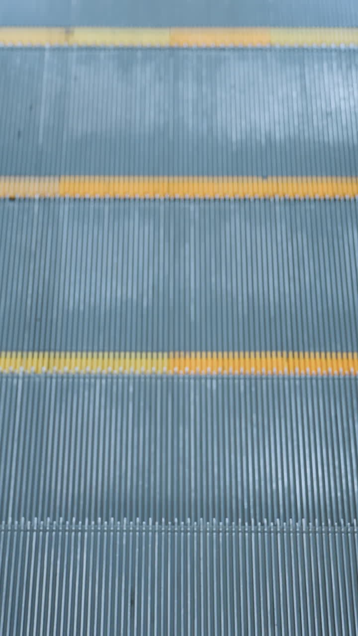 Upward-moving escalator with sleek glass frame, yellow markings, and reflective metal borders in a modern shopping mall, clean, polished design enhances the dynamic urban transport scene