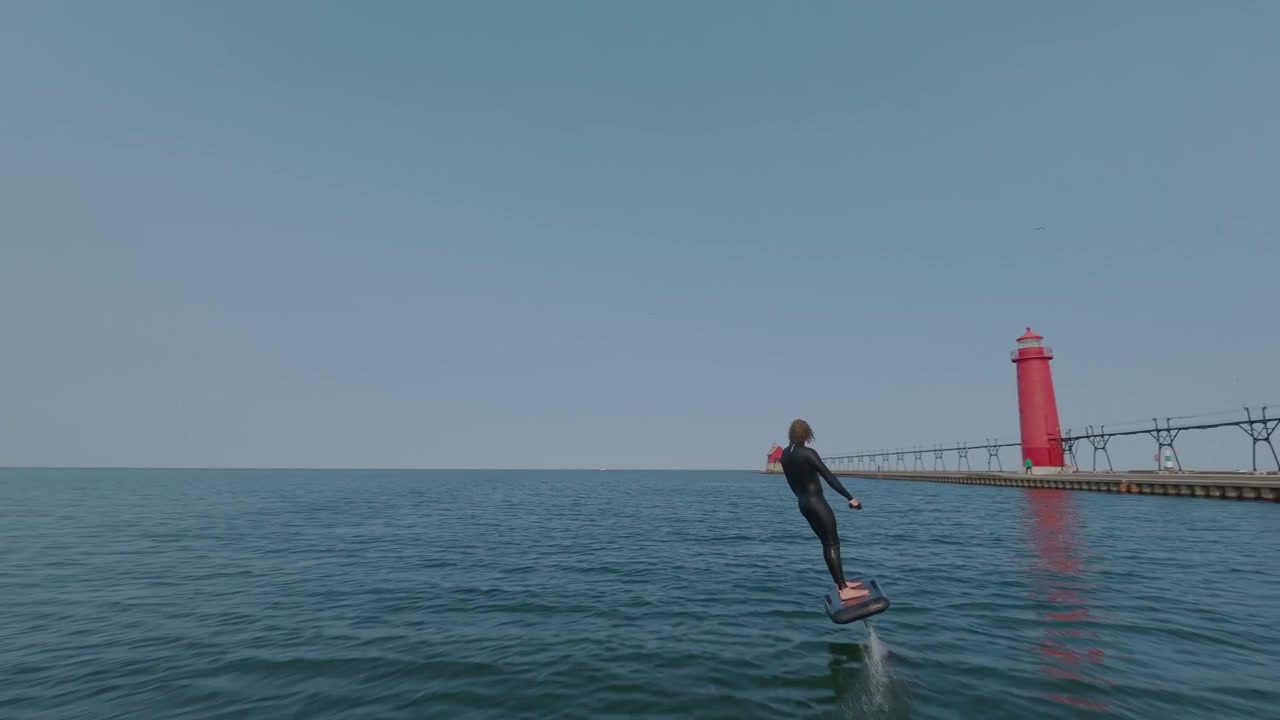 灯台のある穏やかな湖で、ウェットスーツを着た若い男性がeフォイルサーフボードを楽しんでいる。