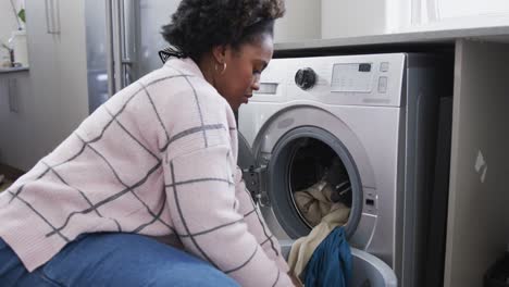 Mujer-Afroamericana-Poniendo-Ropa-En-La-Lavadora,-Lavando-Ropa-En-Casa,-Cámara-Lenta