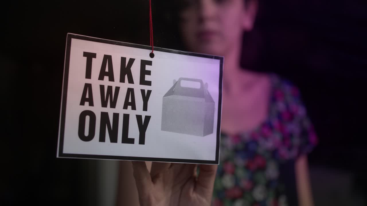 Person Flipping 'Open' Sign to 'Take Away Only' in Shop Window