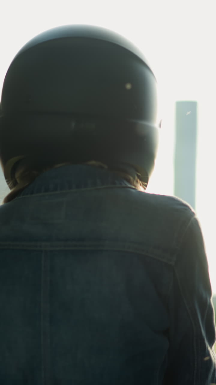 vista trasera de dos mujeres de pie cerca de una ventana, una mirando contemplativa con un fondo de edificio borroso, ambas llevan cascos, la luz crea reflejos suaves