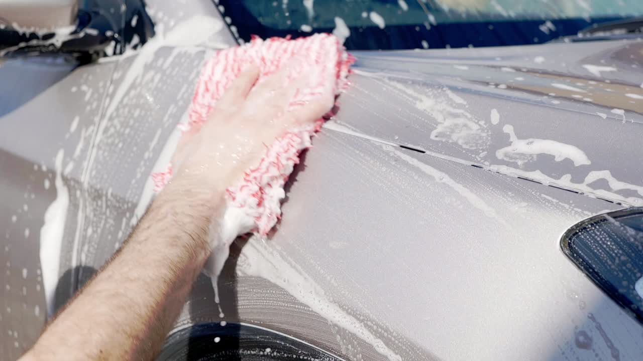 Close up cleaning grey SUV with red microfibre wash mitt and lots of suds