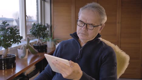middle aged caucasian man reads on a tablet and looks out the window in a hobby room with plants