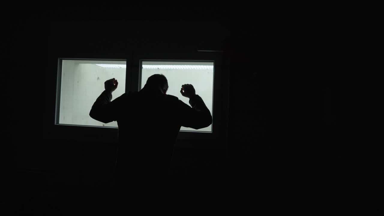 Silhouette suggestiva di un uomo in piedi di fronte a una finestra luminosa, che alza i pugni in segno di frustrazione all'interno di una stanza buia. Ideale per concetti come rabbia, stress, conflitto, isolamento, salute mentale ed emotività