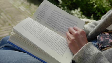 Tiro-De-Cerca-En-Cámara-Lenta-De-Un-Libro-Que-Se-Lee-Y-De-Una-Mujer-Joven-Sentada,-Pasando-Una-Página