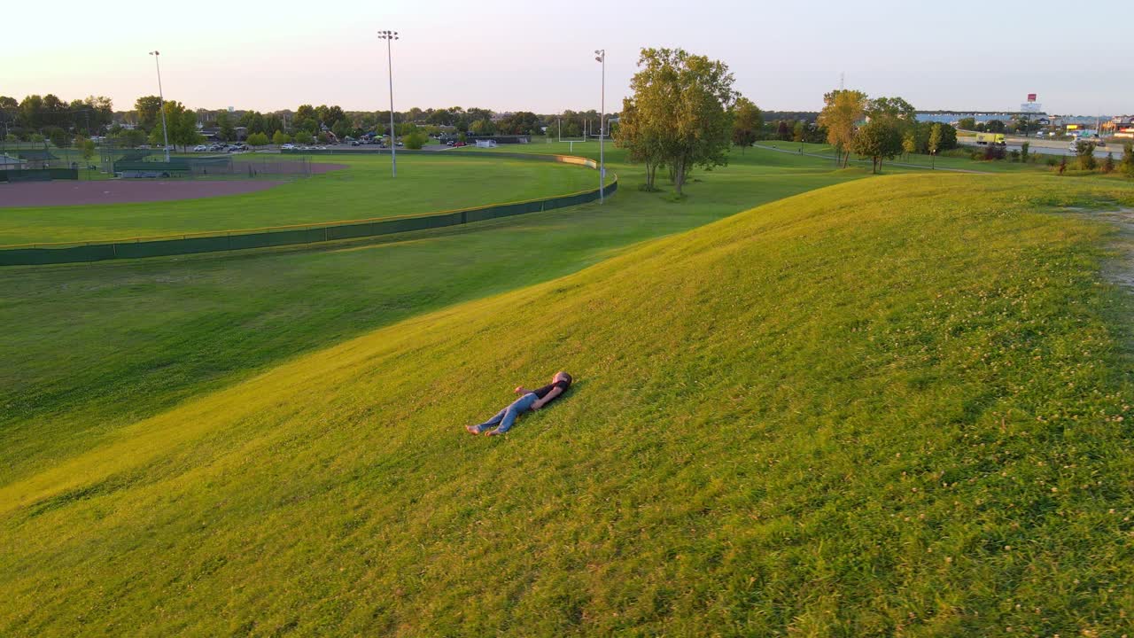 Young boy rolls down small hill with green meadow, side view
