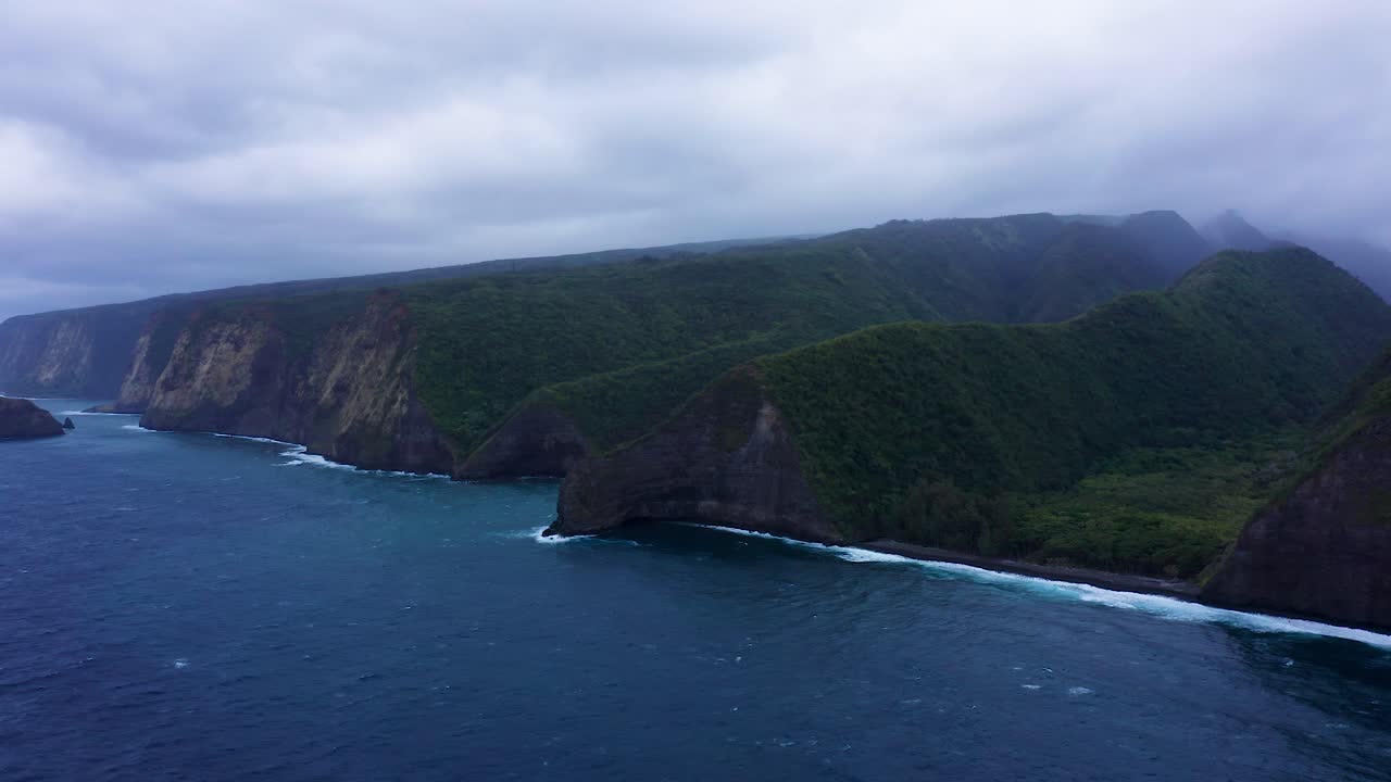 Endless green cliffs disappear into drifting mist, standing above dark rolling waves that meet a remote wild shoreline beneath soft overcast skies.
