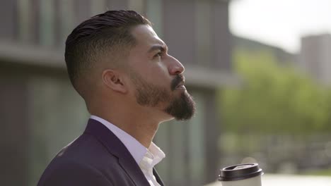 Handsome-focused-businessman-drinking-from-paper-cup-outdoor