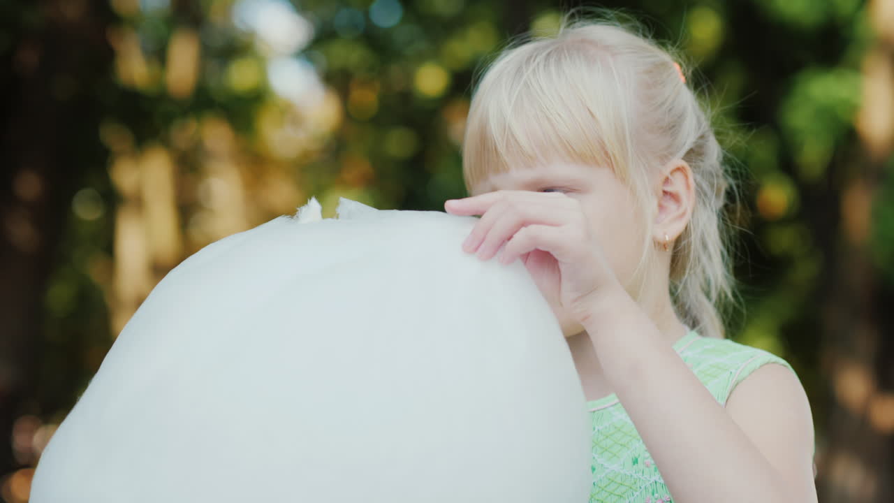 공원에서 달콤한 솜털을 먹고 있는 금발 소녀의 초상화 맑은 여름날 행복한 휴가
