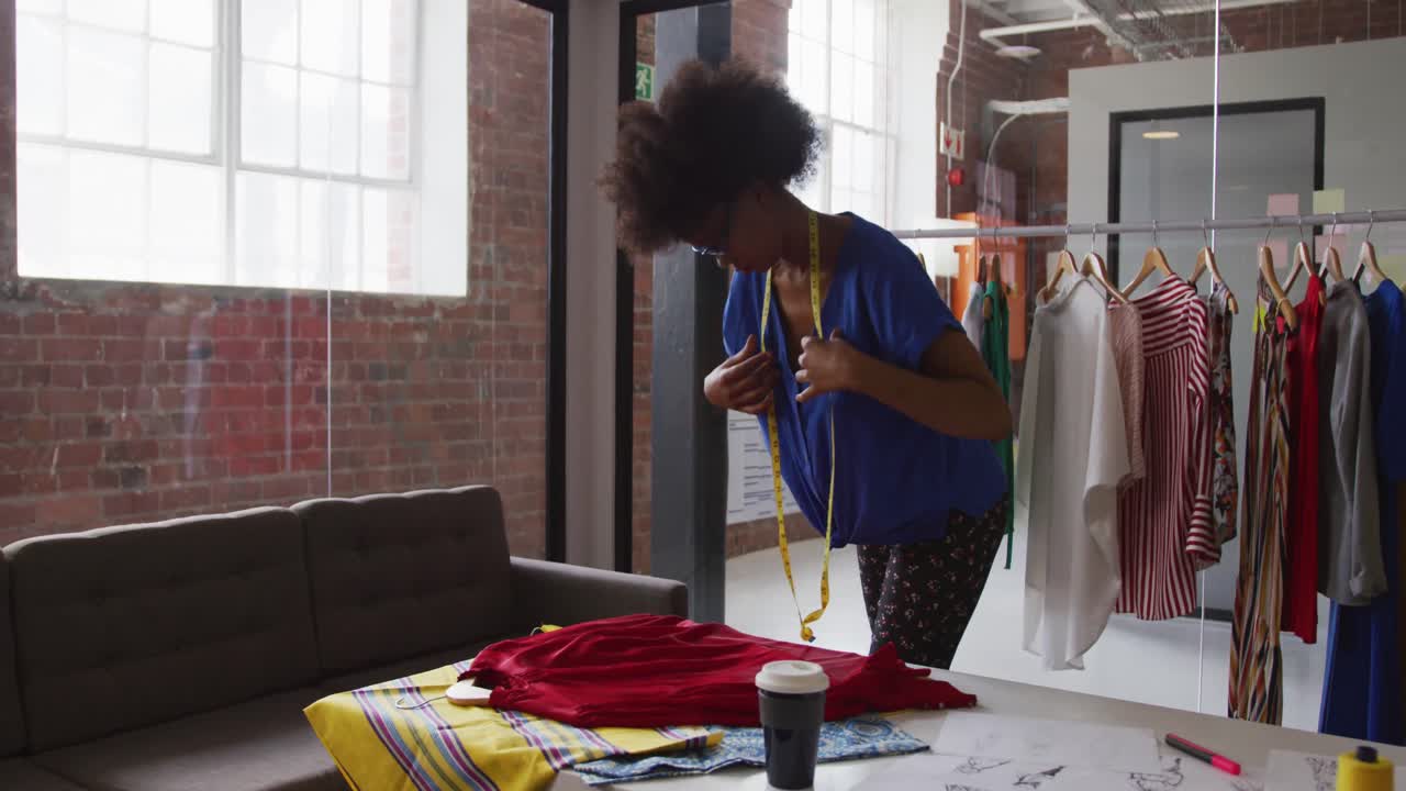 Stilista di moda afroamericana che prende le misure di un capo d'abbigliamento con un metro a nastro.