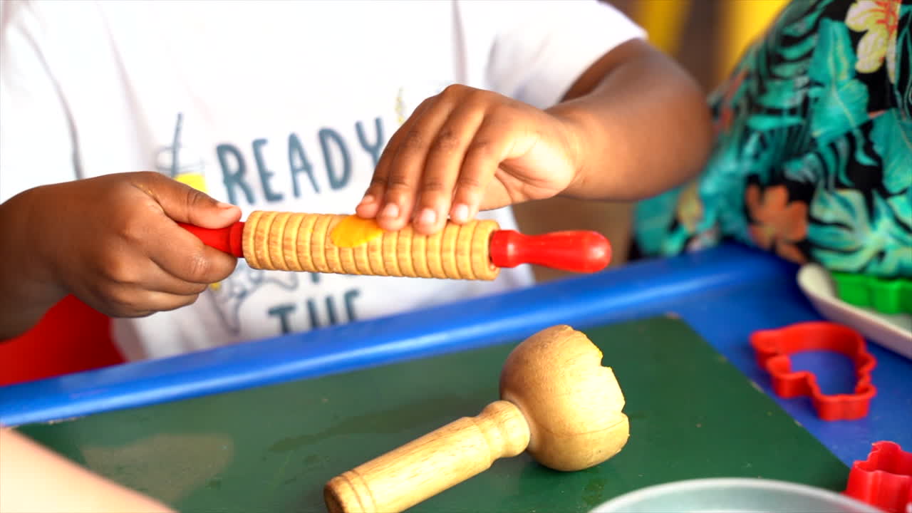 African boy playing with rolling pin and playdough in Montesorri school
