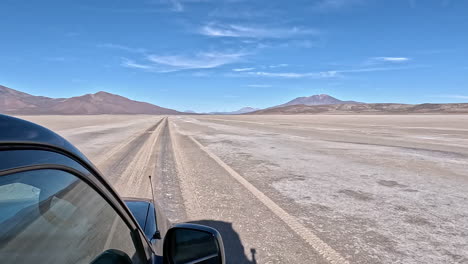 Black-SUV-drives-quickly-across-barren-salt-flats-following-dark-tire-tracks