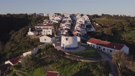 Flying-backwards-at-old-typical-Portuguese-windmill-Odeceixe-during-early-morning,-aerial