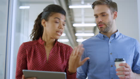 multiethnic people using tablet in office. colleagues talking while walking.