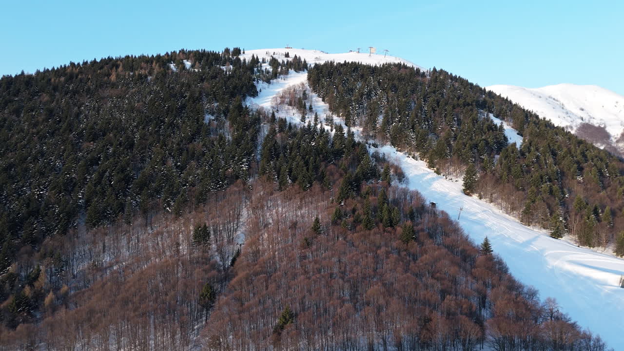 Aerial view of snowy mountain with forested slopes and ski trails