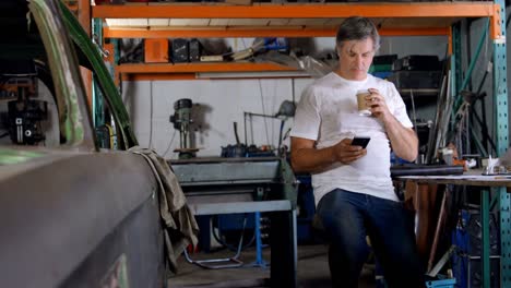 Männlicher-Mechaniker-Trinkt-Kaffee,-Während-Er-Das-Mobiltelefon-4k-Benutzt
