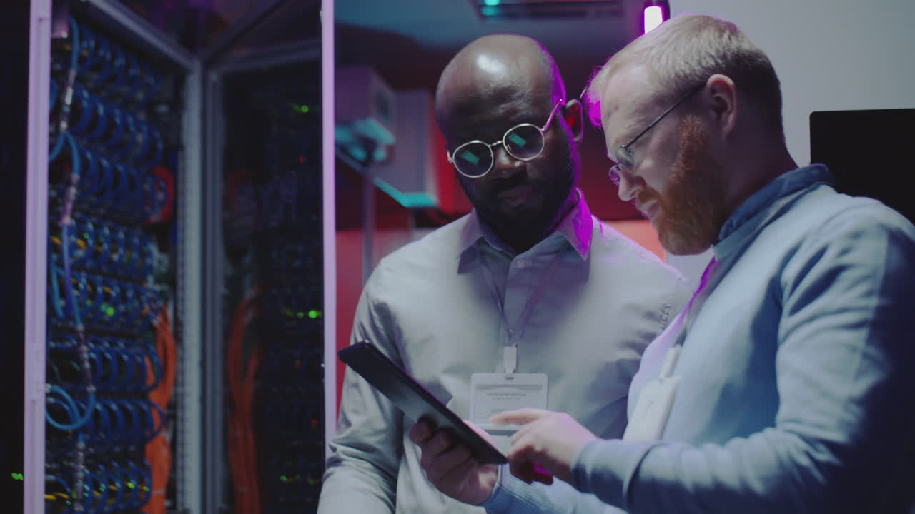 Two IT professionals examine a tablet in a server room
